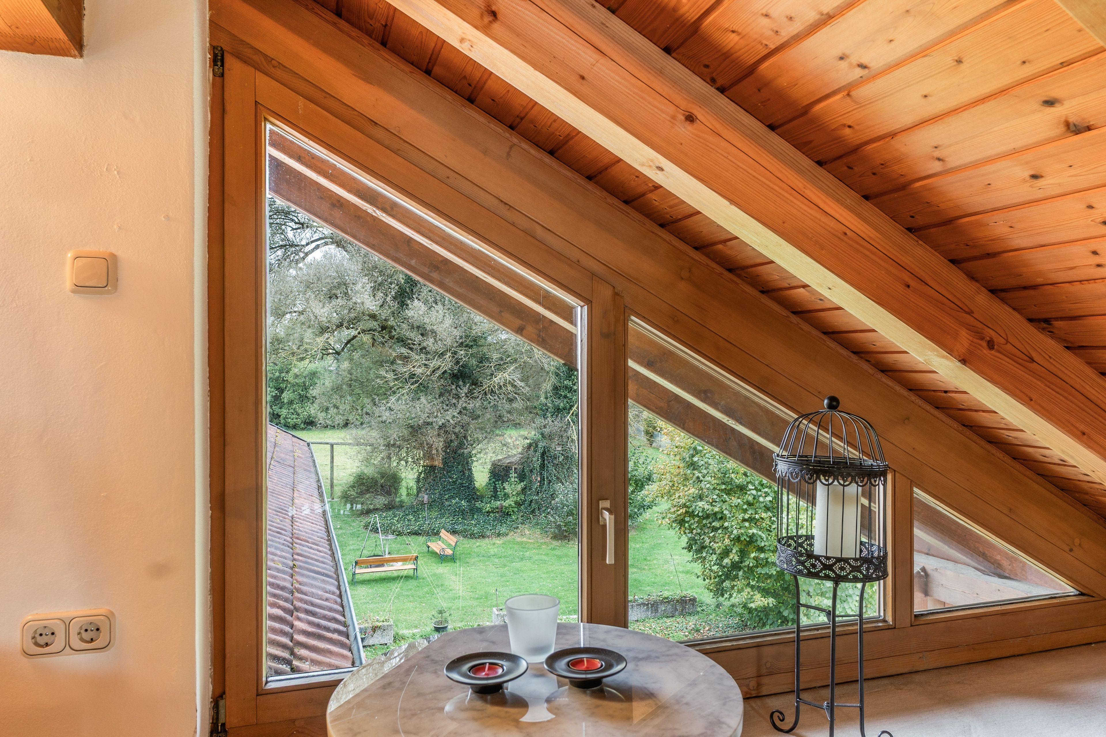 Une pièce avec un plafond en pente, de grandes fenêtres, une table décorée de bougies et une cage à oiseaux.