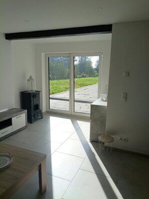 A spacious room with a large sliding glass door leading to an outdoor area, a wooden table, and a small seating area. - New! Meerzeit Vacation Home (Nenndorf)