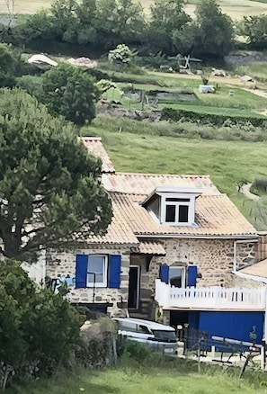 A stone house with a tiled roof, a small balcony, and a car parked in front.