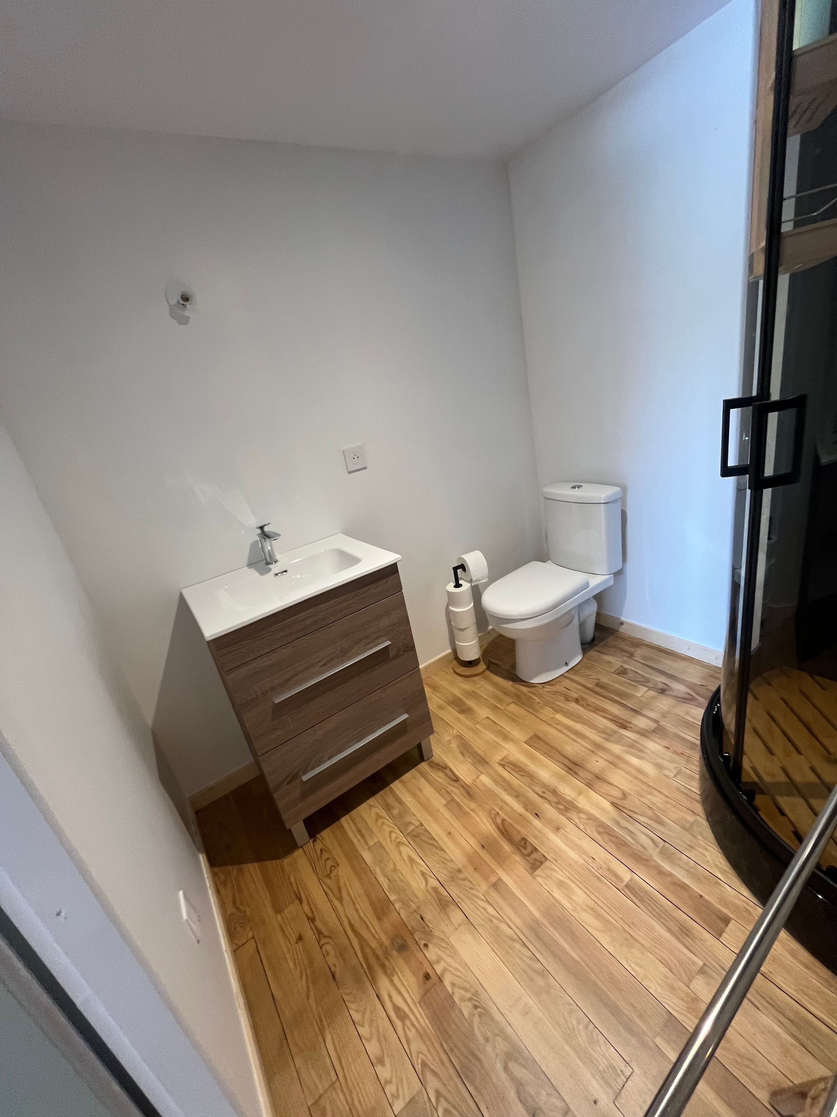 A bathroom with a wooden floor, white walls, a white sink, and a toilet.