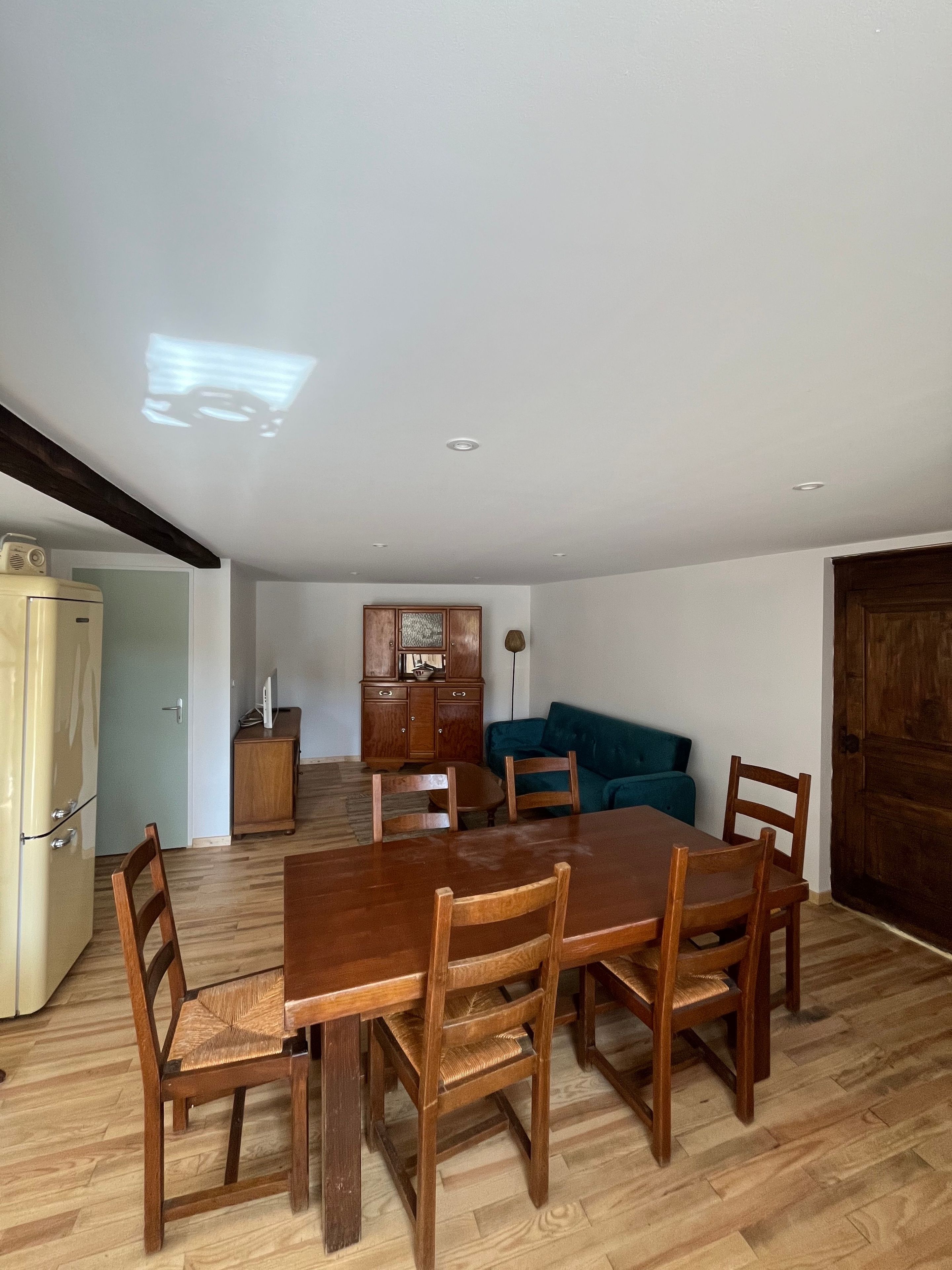 A dining area with a wooden table and chairs, a kitchen with cabinets, and a blue sofa in the background.