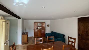 A dining area with a wooden table and chairs, a kitchen with cabinets, and a blue sofa in the background.