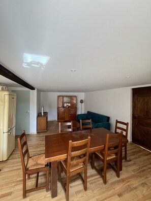 A dining area with a wooden table and chairs, a kitchen with cabinets, and a blue sofa in the background.
