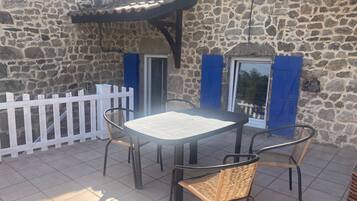 Un edificio de piedra con un patio empedrado, una valla blanca y una mesa con sillas.