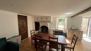 A dining area with a wooden table and chairs, a kitchen with a window, and a stone wall outside.