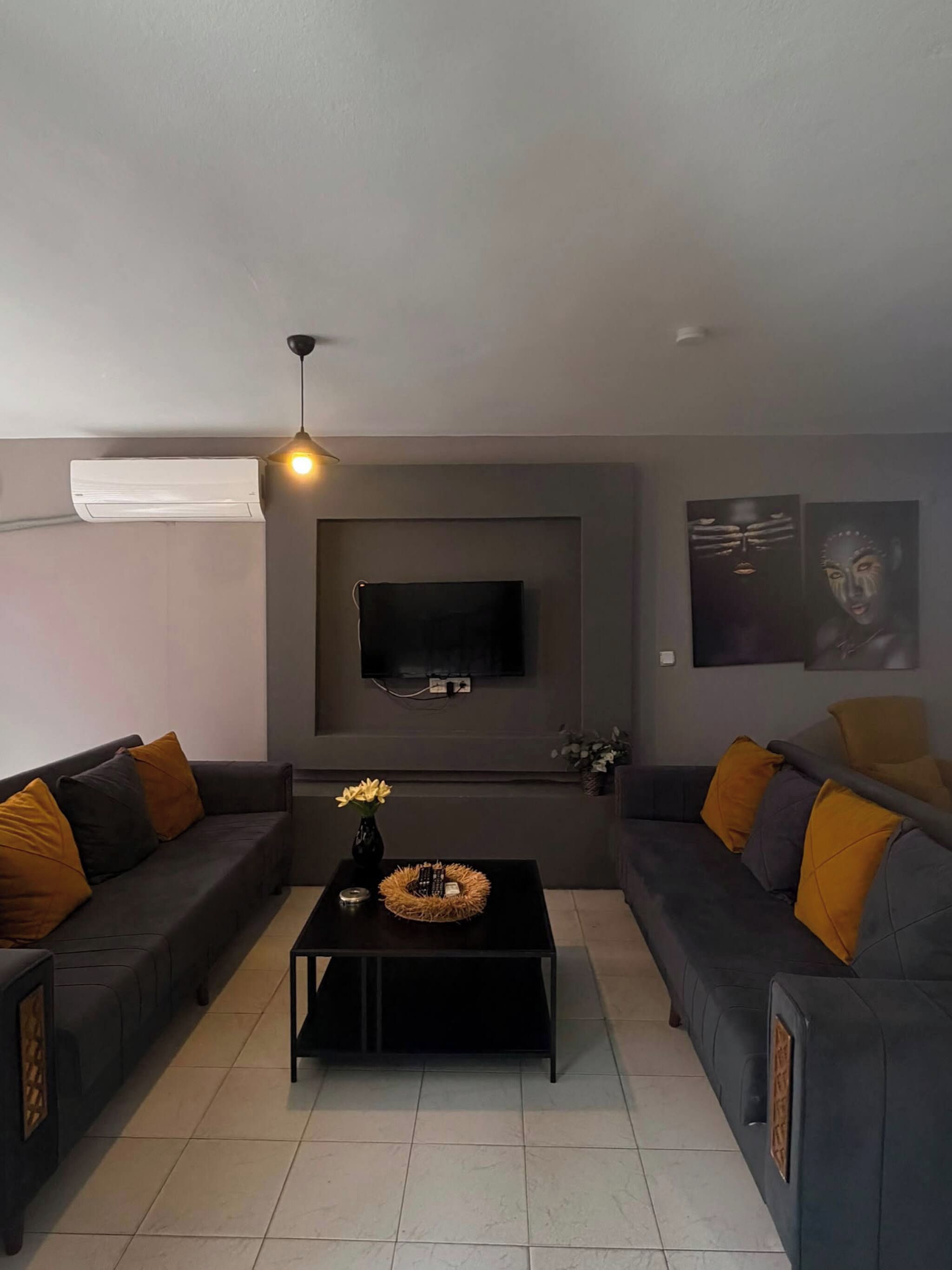 A modern living room with two sofas, a coffee table, a flat-screen TV mounted on the wall, and a pendant light.