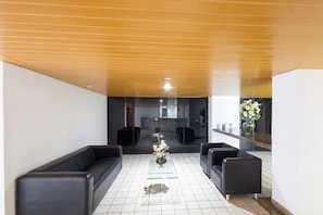 A reception area with a reception desk, black leather sofas, a vase with flowers, and a tiled floor. - Design Apartment 100m From the Beach Min0709 (Maceió)
