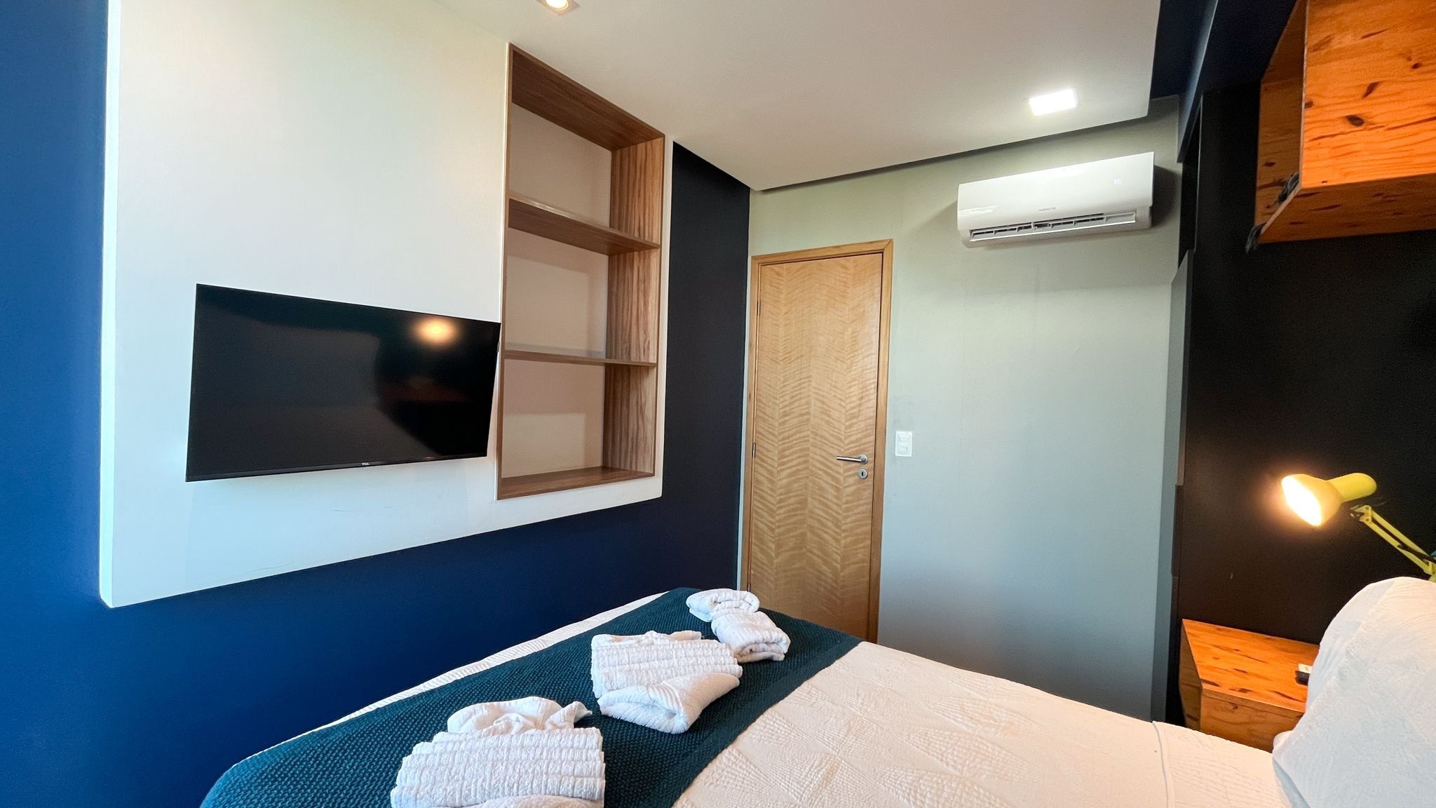 Ein Hotelzimmer mit einem Bett, einem Flachbildfernseher an der Wand, einer Holztür und einer Klimaanlage.