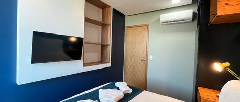 Ein Hotelzimmer mit einem Bett, einem Flachbildfernseher an der Wand, einer Holztür und einer Klimaanlage.