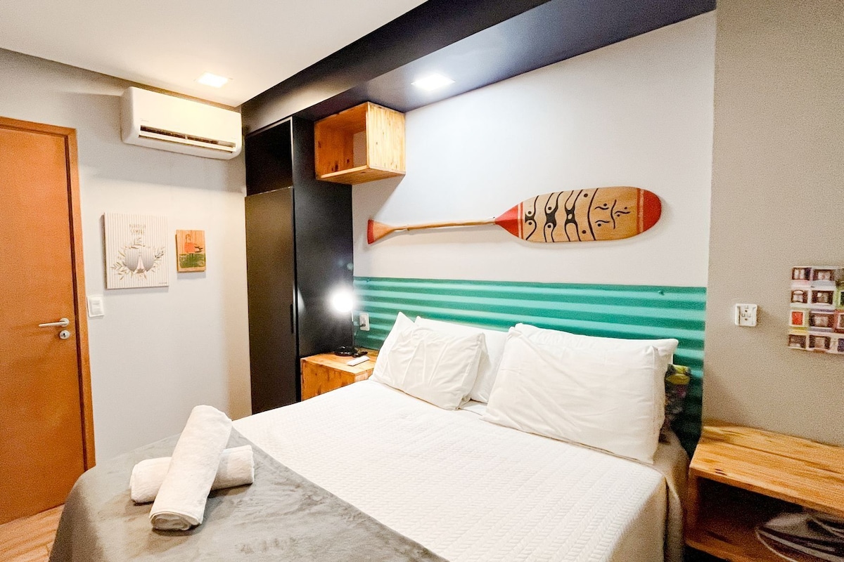A hotel room with a bed, a wooden paddle wall art, a door, and an air conditioning unit.