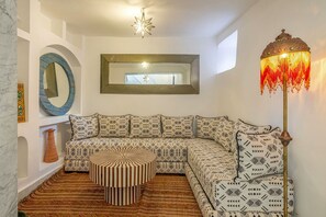 A modern living room with a sectional sofa, a round ottoman, a floor lamp, and a large mirror on the wall. - Riad mama latifa (Marrakech)