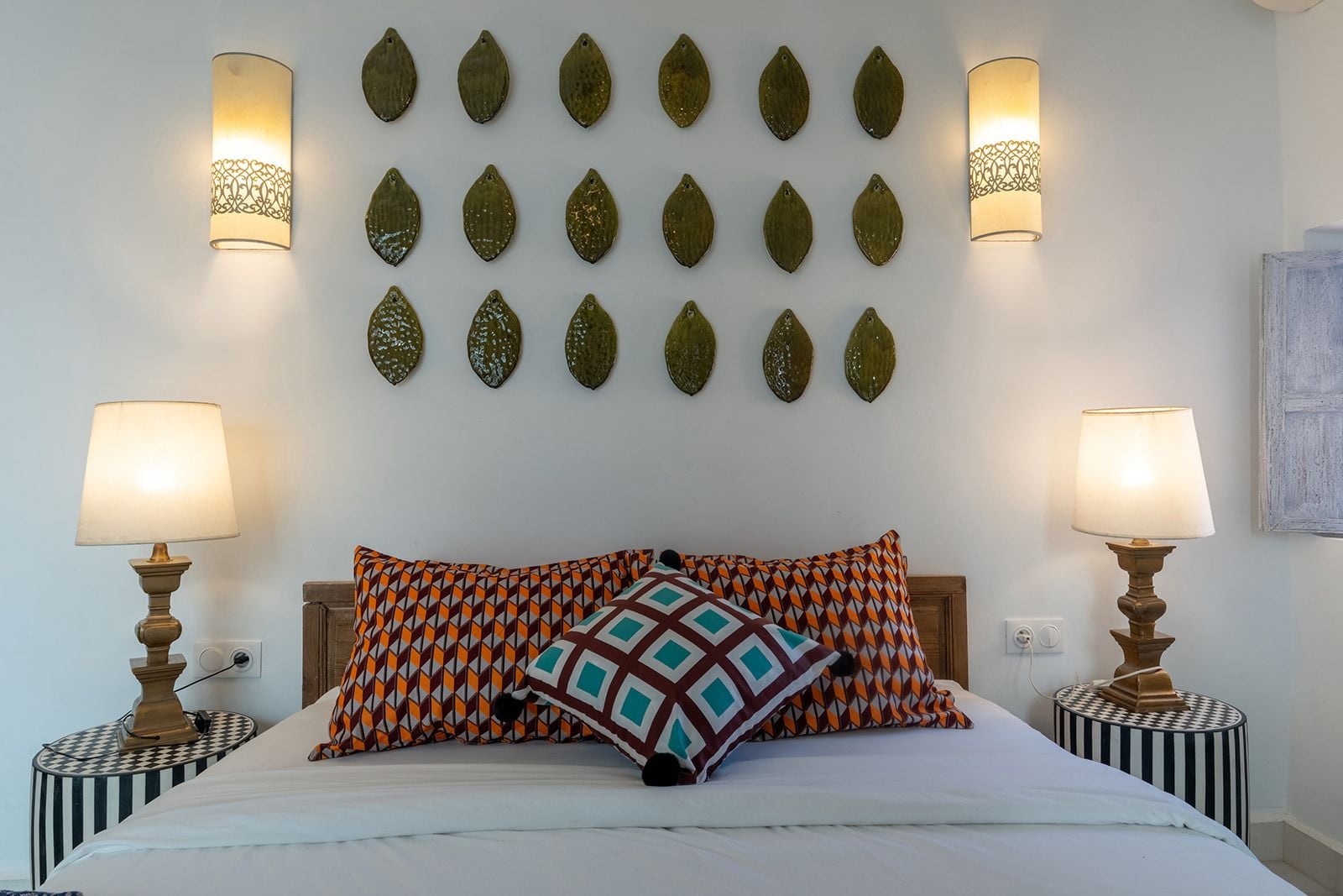 A bed with patterned pillows, two bedside lamps, and decorative wall art.