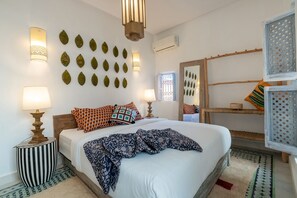 A bedroom with a bed, bedside lamps, decorative wall art, a window, and a wooden ladder. - Riad mama latifa (Marrakech)