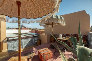 A rooftop terrace with a patterned umbrella, a cactus plant, and a table with cushions. - Riad mama latifa (Marrakech)