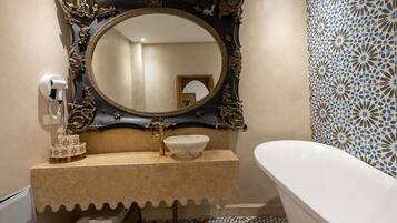 Une salle de bain dotée d’un grand miroir décoratif, d’un lavabo blanc avec un robinet doré et d’une baignoire blanche.