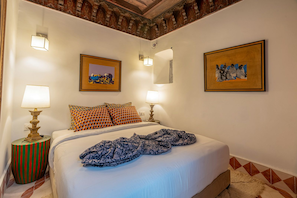 A hotel room with a bed, two bedside lamps, patterned pillows, a framed picture above the bed, and a patterned rug on the floor. - Riad mama latifa (Marrakech)