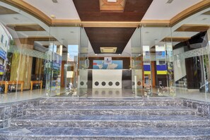 Vestíbulo de hotel con una escalera de mármol, paredes de vidrio y una recepción.