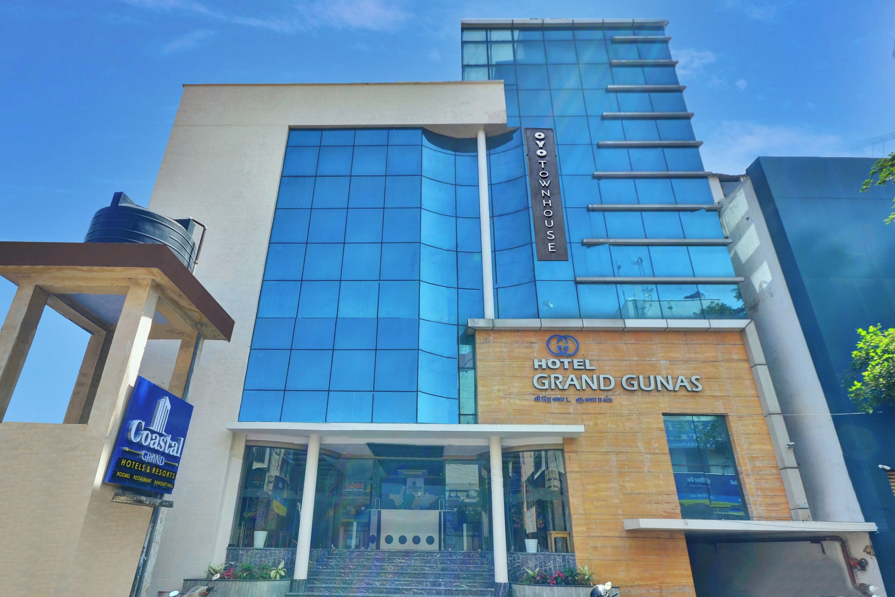 Un hotel con fachada moderna, un letrero llamativo que dice 'Hotel Grand Gunas' y una entrada visible con escalones que conducen a las puertas principales.