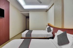 A hotel room with two beds, a television on the wall, and a ceiling light.