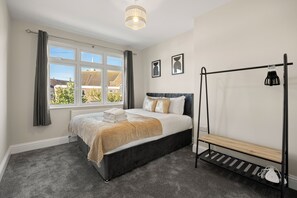 Een slaapkamer met een bed, een raam, een radiator, een nachtkastje en een kledingrek.