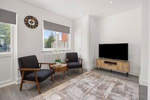 Een moderne woonkamer met twee fauteuils, een ronde salontafel, een flatscreen-televisie op een houten tv-meubel en een groot raam met uitzicht.