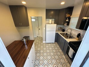 A compact kitchen with dark cabinets, a white refrigerator, a patterned floor, and a sink with a knife block. - South Park’s Better Half (San Diego)