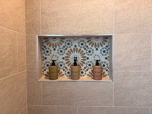 A bathroom with a tiled wall and a shelf containing three bottles of toiletries. - South Park’s Better Half (San Diego)