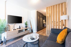 A modern living room with a flat-screen TV, a coffee table with remote controls, a sofa with a yellow pillow, and a wooden partition. - Newlands Peak Studio with AC and gym (Cape Town)