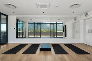 A spacious room with large windows, a black exercise mat in the center, and an exit sign on the wall. - Newlands Peak Studio with AC and gym (Cape Town)