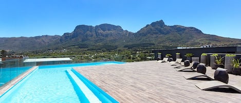 A swimming pool with a view of mountains, lounge chairs, and potted plants.