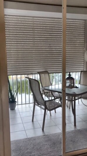 A dining area with a table and chairs, a potted plant, and a view through a window with blinds. - Remodeled 2BR/2BR Ft Myers condo: Large lenai w/lake view, pool, gym, cov prkng (Fort Myers)
