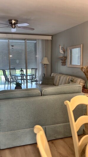 A living room with a grey sofa, a ceiling fan, and a dining area with chairs and a table. - Remodeled 2BR/2BR Ft Myers condo: Large lenai w/lake view, pool, gym, cov prkng (Fort Myers)