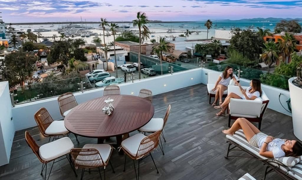 A rooftop terrace with a dining table and chairs, a lounge area with a sofa, and a view of the marina and beach.