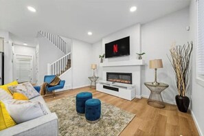 A modern living room with a fireplace, a flat-screen TV, a staircase, and a blue armchair. - Spacious Family Home In Orchards | Near Airport (Edmonton)