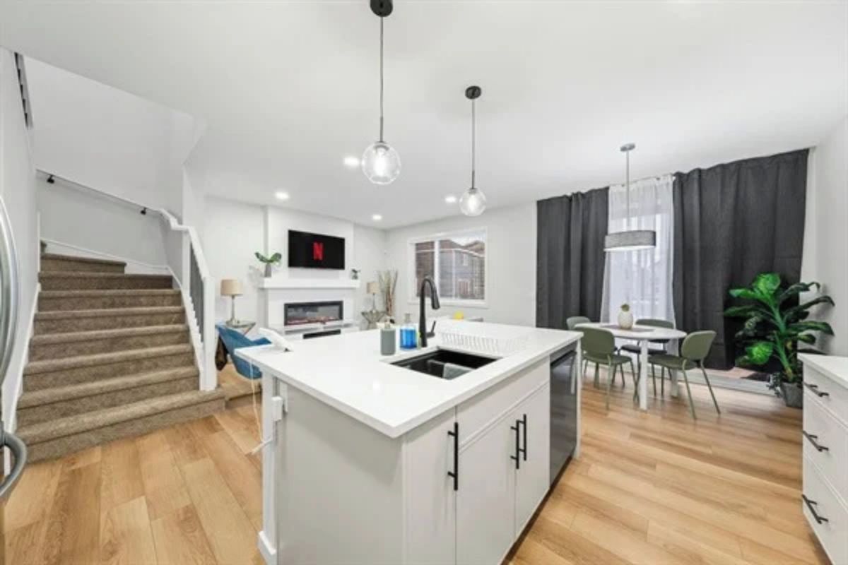 A modern apartment with a kitchen island, dining area, and a staircase leading to a loft.