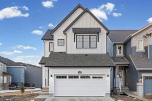 A two-story residential house with a garage, a small front porch, and a clear sky. - Spacious Family Home In Orchards | Near Airport (Edmonton)