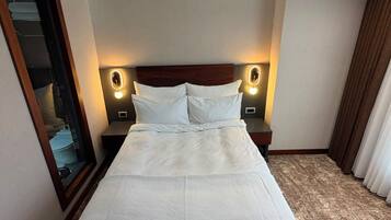 Habitación de hotel con una cama grande, dos lámparas de noche, un espejo y suelo alfombrado.