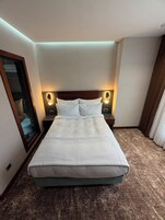 A hotel room with a large bed, two bedside lamps, a mirror, and a carpeted floor.
