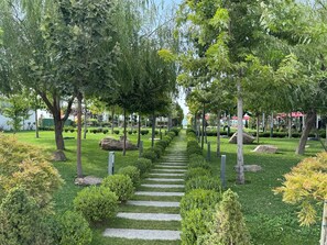A landscaped garden with a stone pathway, trees, and neatly trimmed bushes. - Venedik Otel (Van)