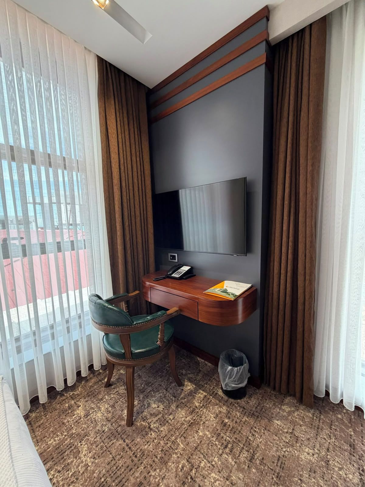 A hotel room with a desk, chair, TV, and a view through the window.