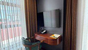A hotel room with a desk, chair, TV, and a view through the window.