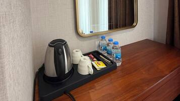 Habitación de hotel con una mesita de noche de madera, una bandeja negra con tetera, tazas y agua embotellada.