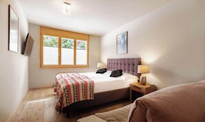 A bedroom with a bed, bedside table, lamp, and a window with blinds. - 3-BEDROOM ZERMATT RETREAT WITH TERRACE & WELLNESS ACCESS (Zermatt)