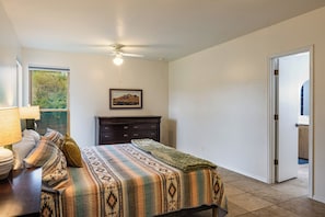 Un dormitorio con cama, cómoda, ventilador de techo y ventana con vista a árboles.