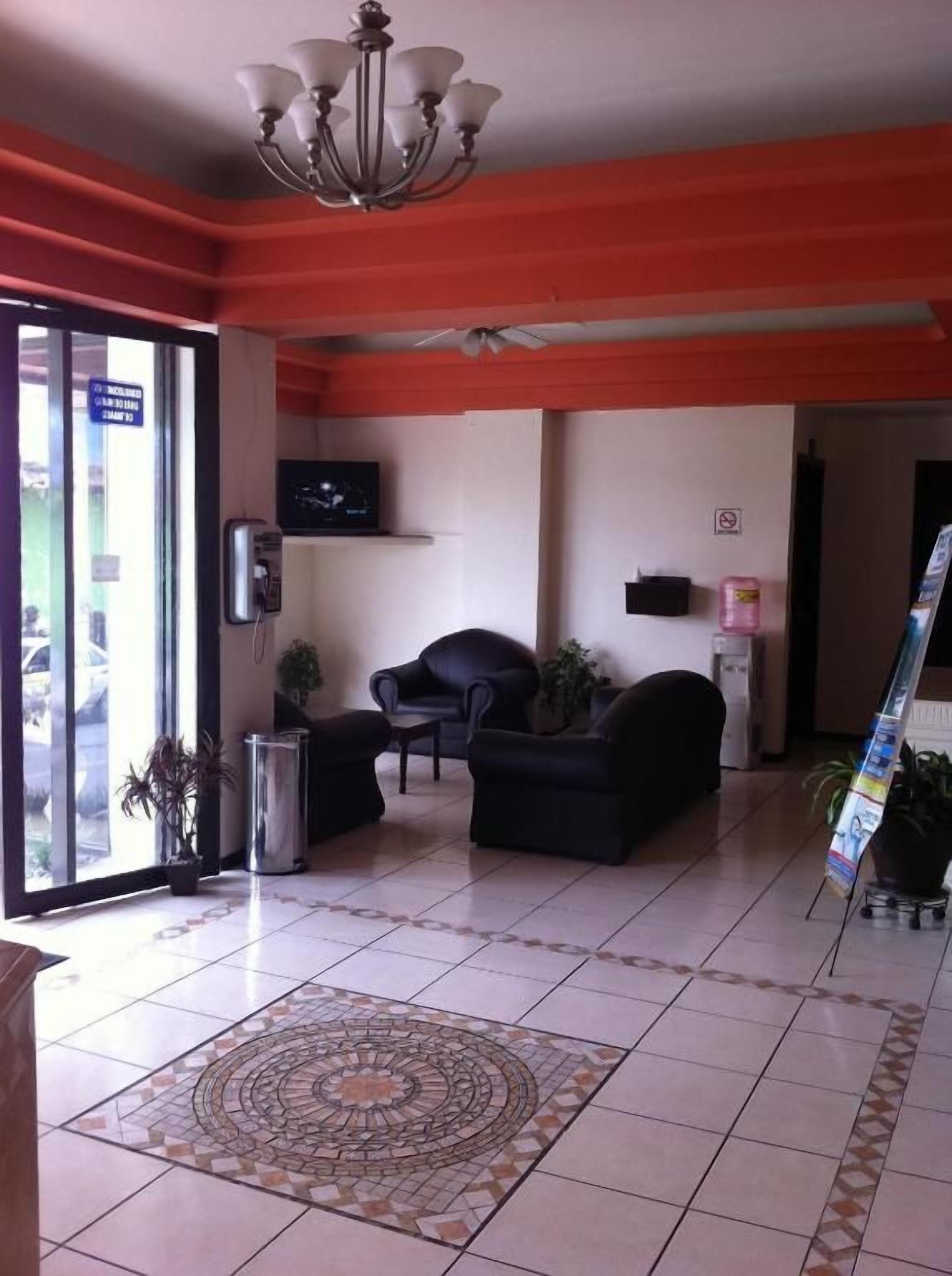 A lobby with a tiled floor, a chandelier, a sofa, a television, and a plant.