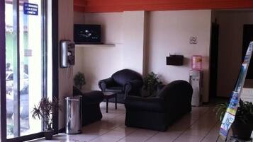 A lobby with a tiled floor, a chandelier, a sofa, a television, and a plant.