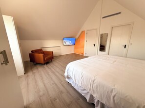 Ein Schlafzimmer mit einem großen Bett, einem Sofa, einem Fernseher und einer Treppe, die zu einem Erker führt.