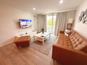 Ein modernes Wohnzimmer mit Flachbildfernseher, einer Couch, einem Couchtisch und einer Schiebetür zu einem Balkon.