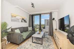 A modern living room with a grey sofa, a coffee table, a TV, and a balcony with a view. - Newlands Peak Studio with Gym (Cape Town)