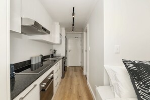 A narrow kitchen with white cabinets, a black countertop, and a wooden floor. - Newlands Peak Studio with Gym (Cape Town)